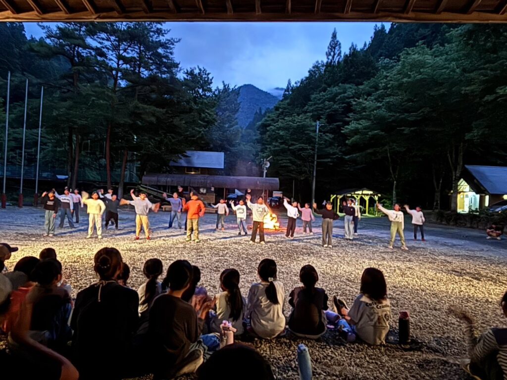 キャンプファイヤーを囲んでスタンツを披露する子どもたち